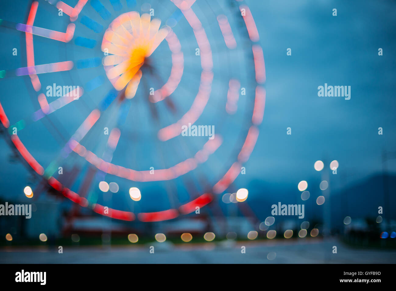 Abstract sfocatura di immagine colorata luminosamente illuminata ruota panoramica Ferris nella città di divertimenti Parco su nero blu del cielo della sera Bokeh di fondo Foto Stock