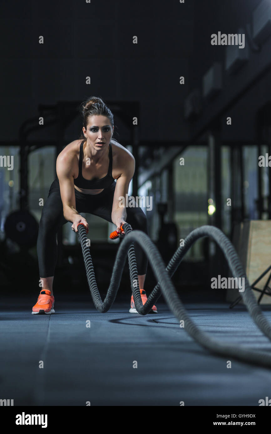 Concetto: Potenza, forza, uno stile di vita sano, sport. Potente attraente donna muscolare CrossFit trainer battaglia allenamento con r Foto Stock