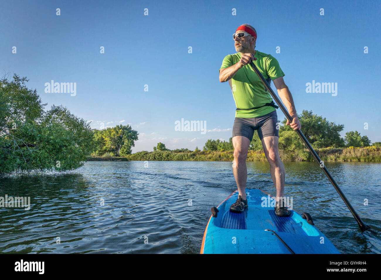 Muscolare, senior paddling maschio un stand up paddleboard sulle sponde di un lago in Colorado Foto Stock