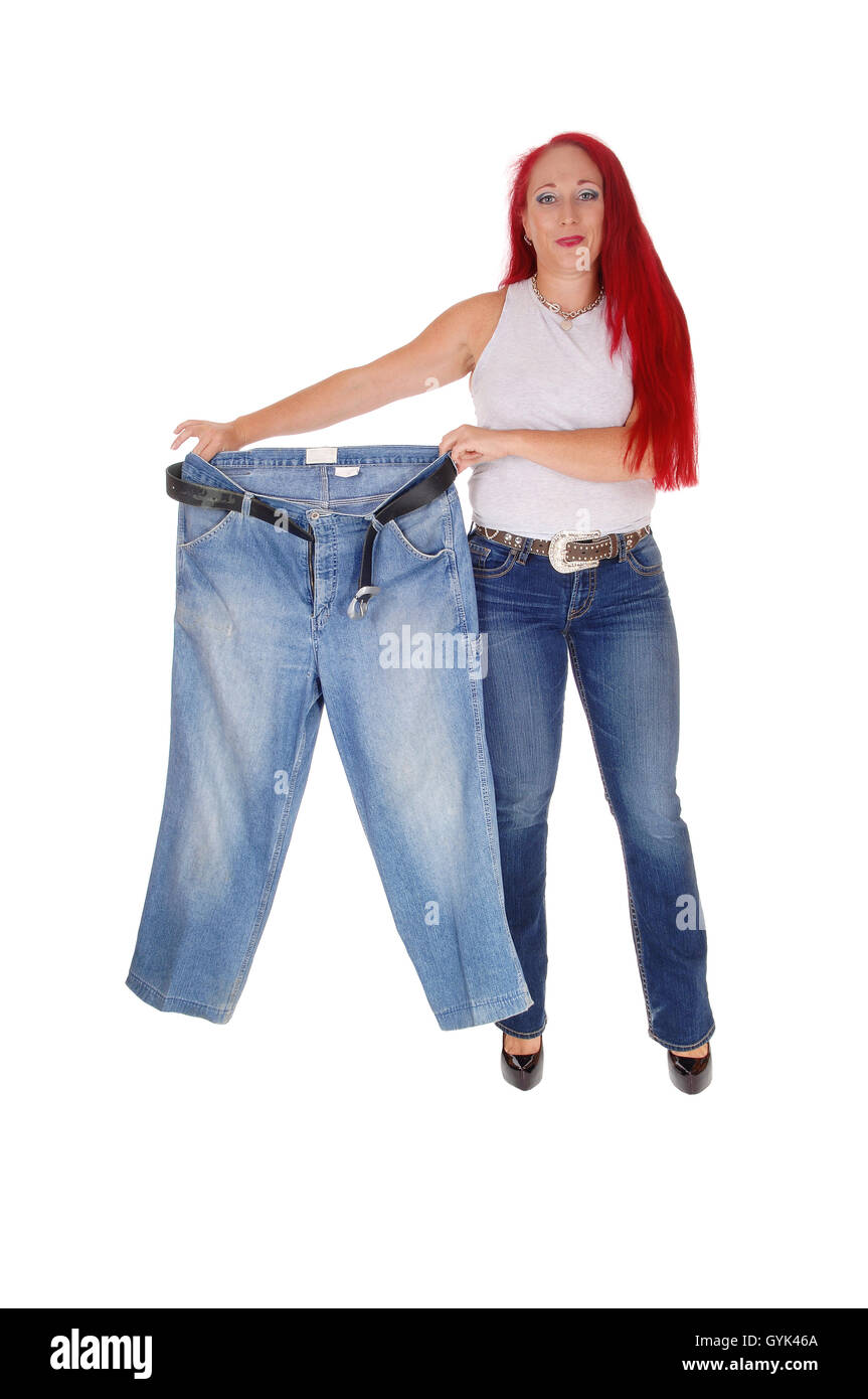 Un tall woman tenendo in mano il suo vecchio jeans grandi mostrando la sua perdita di peso con lunghi capelli rossi, isolato per sfondo bianco. Foto Stock