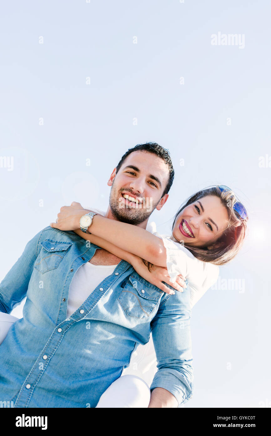 Giocoso giovane godendo le loro vacanze estive come l'uomo porta la donna piggyback Foto Stock