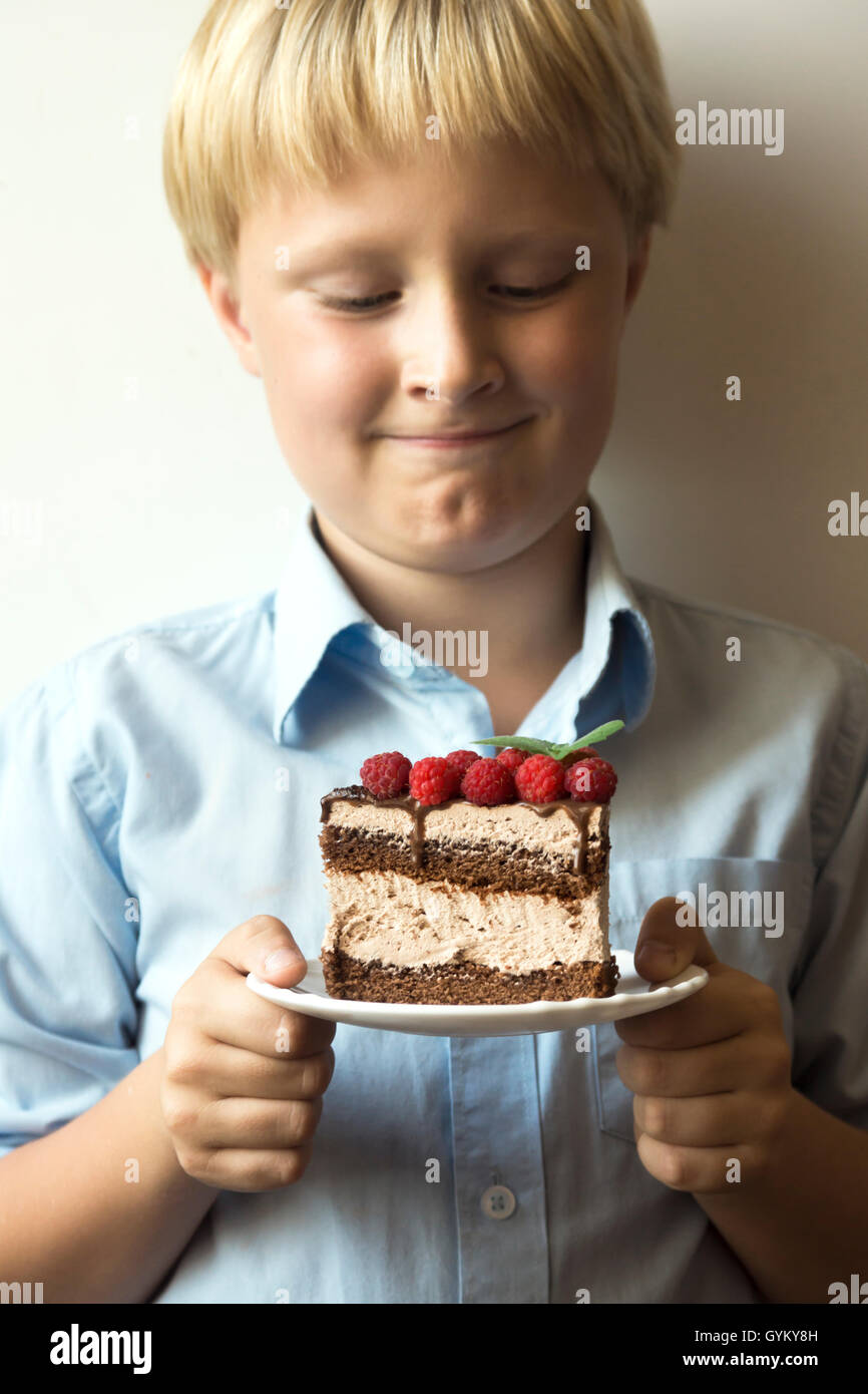 Torta in mani - sorridendo felice ragazzo (kid, bambino, adolescente) tenendo in mano la piastra con un pezzo di delizioso cioccolato artigianale e r Foto Stock
