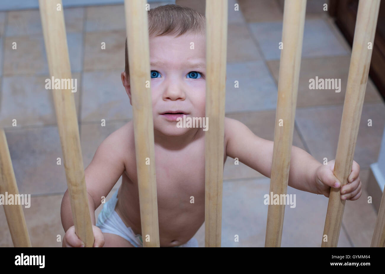 Un anno di età baby boy dietro il legno porta di sicurezza di scale. Egli sta cercando di andare al piano di sopra Foto Stock