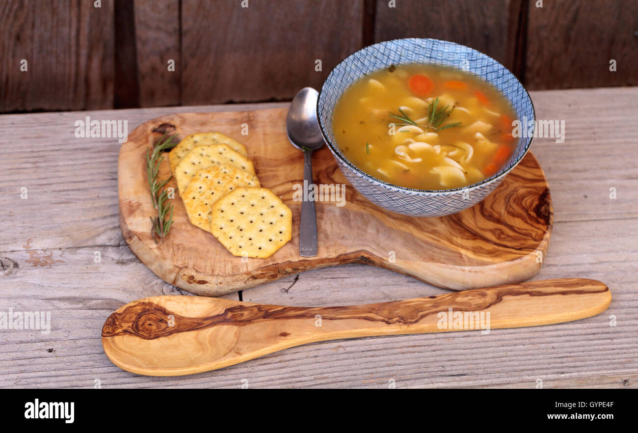 Zuppa di noodle al pollo in azzurro e bianco ciotola con cracker, tutti seduti su un legno tagliere. Foto Stock