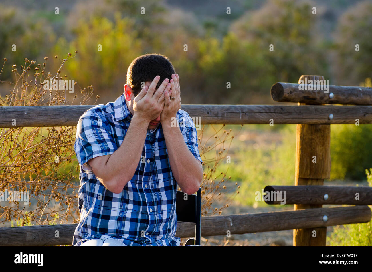 L'uomo sconvolto con la testa tra le mani seduti all'aperto con un campo vibrante in background. Foto Stock