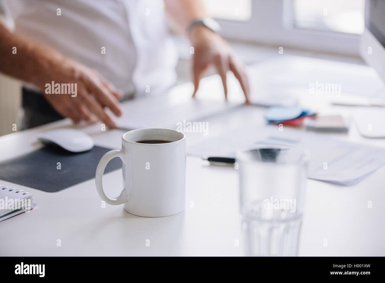 Immagine ravvicinata di tazza di caffè fresco sulla scrivania con uomo che lavora in background. Foto Stock