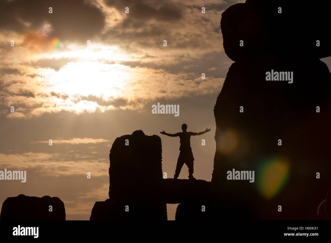 Il solstizio d'Estate a Stonehenge, Wiltshire, Regno Unito e come il sole sorge segnando l'inizio del giorno più lungo dell'anno, Giugno 21st, la silhouette di un uomo, con le braccia sollevate in omaggio al Rising Sun può essere visto come egli si erge sulla cima di una delle antiche pietre dove la folla si riuniscono ogni anno per testimoniare l'evento. Foto Stock