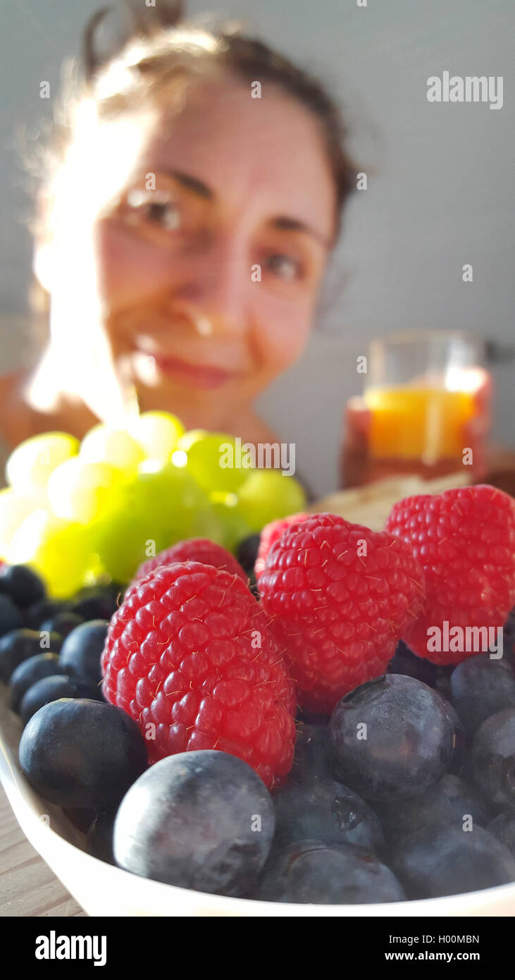 Unione rosso lampone (Rubus idaeus), la donna che guarda in avanti per una coppa di frutta con lamponi, bluberries e uva, dessert di frutta, Germania Foto Stock