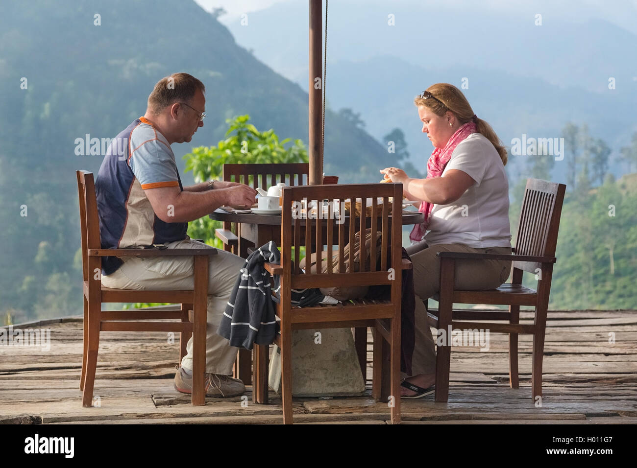 ELLA, SRI LANKA - Marzo 3, 2014: turista giovane avente la colazione al bungalow terrazza con straordinaria vista sulle piantagioni di tè in bac Foto Stock