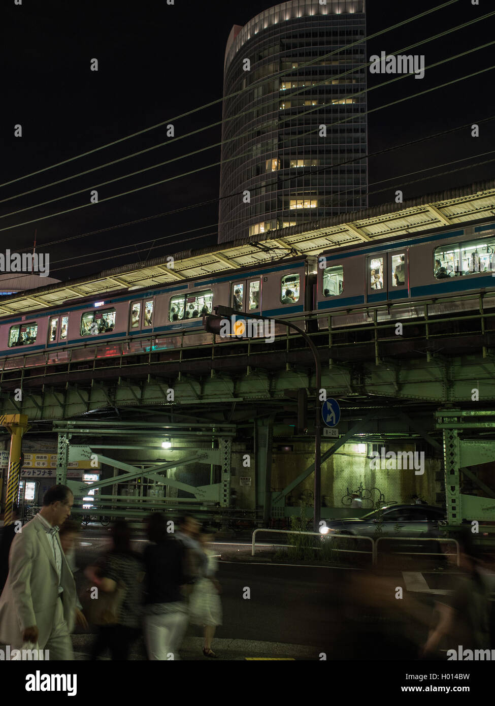 I pedoni a piedi sulla trafficata strada notte sotto la linea Yamanote treno passeggeri alla stazione di Yurakucho, Tokyo, Giappone Foto Stock