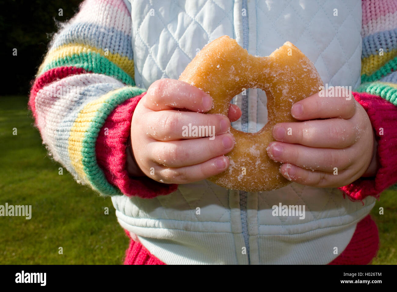 Un bambino piccolo con dita appiccicose di mangiare un enorme ciambella. Foto Stock