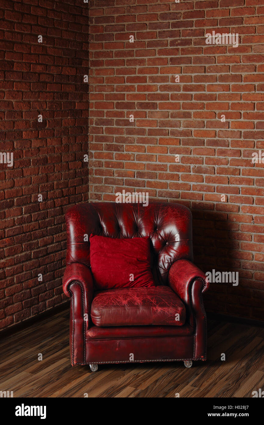 Vecchio rosso scuro poltrona in pelle in un angolo della stanza con un muro di mattoni. Foto Stock