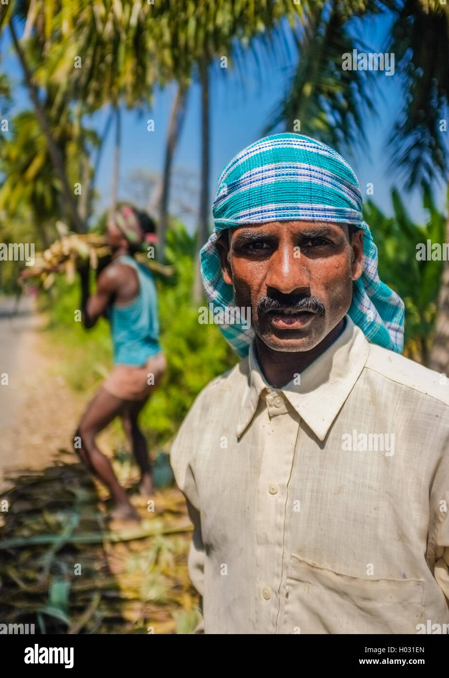 HAMPI, India - 28 gennaio 2015: Ritratto di lavoratore indiano con secondo lavoratore di canna da zucchero di carico sul carrello Foto Stock