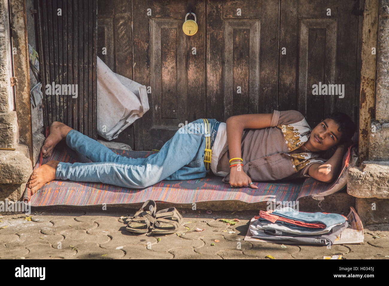 MUMBAI, India - 10 gennaio 2015: giovani indiani uomo in street si appoggia sul tappetino nella parte anteriore della porta. Post-elaborati con grano, una texture Foto Stock