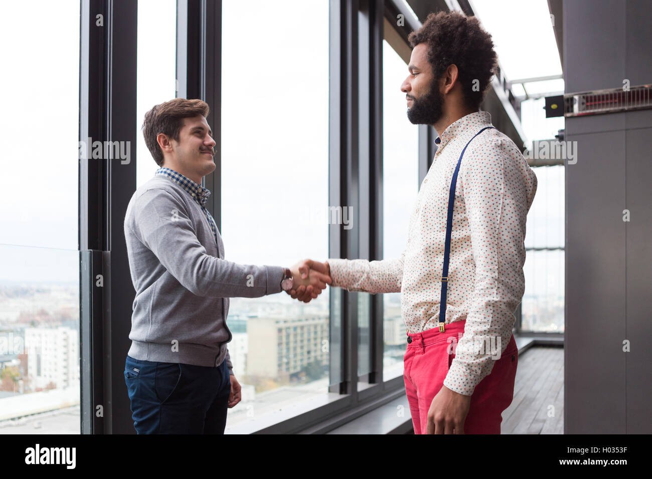 Due giovani imprenditori stringono le mani in un ufficio moderno hall. Foto Stock
