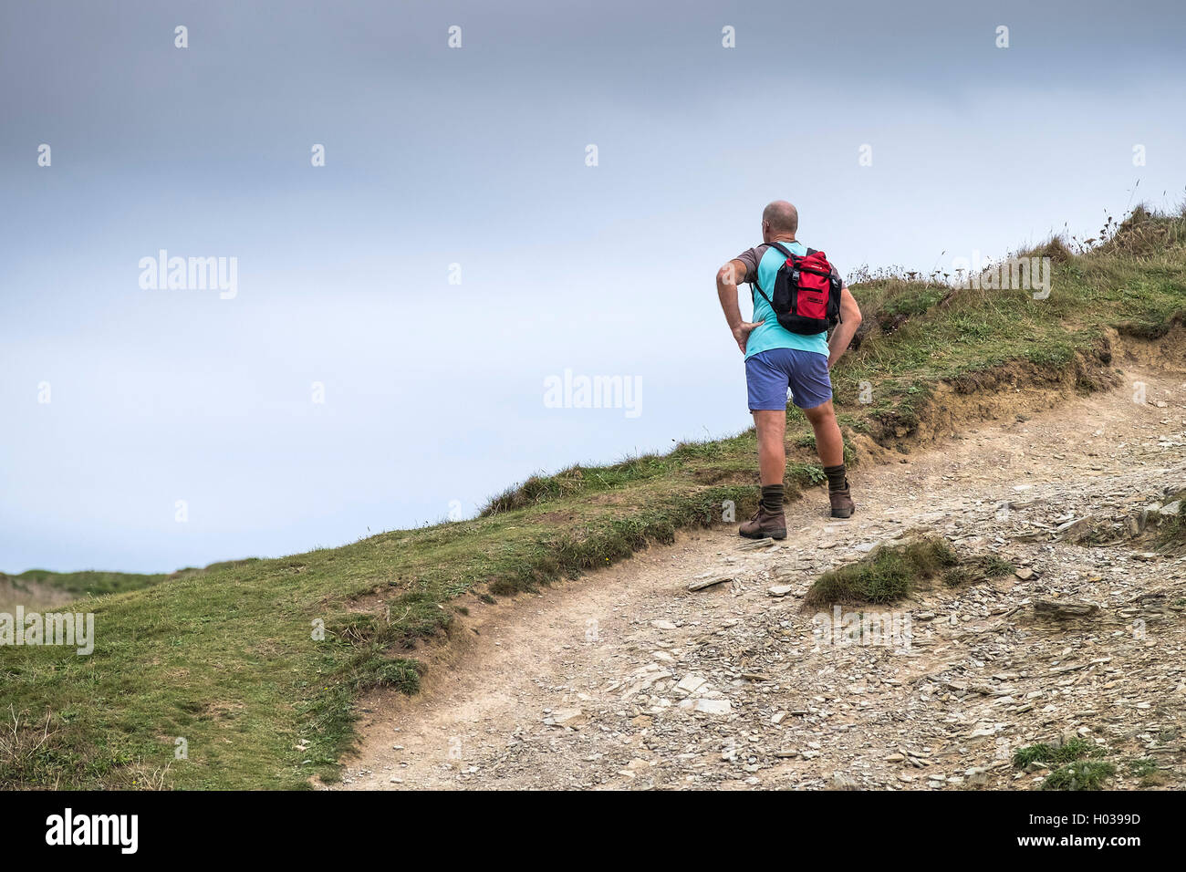Un viandante prende un periodo di riposo e gode della vista di come egli cammina lungo il sud ovest via costiera in Cornovaglia. Foto Stock