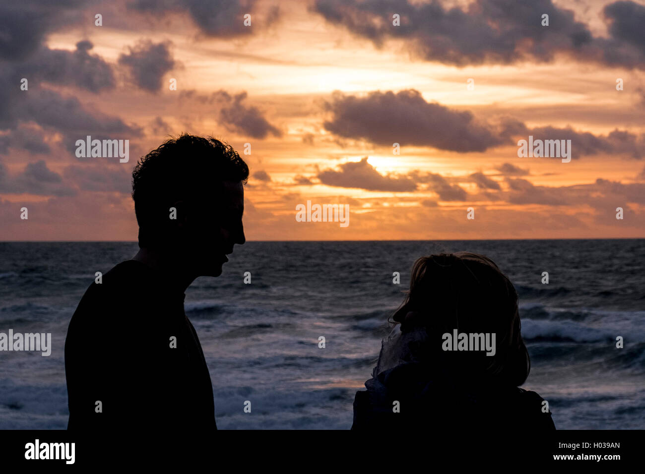 La silhouette di un paio di chat come il sole tramonta alle Fistral Beach in Newquay, Cornwall. Foto Stock