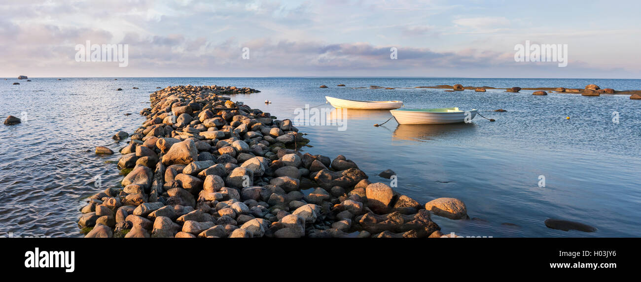 Due bianchi oaring barche dietro di ciottoli molo di pietra in mare al tramonto Foto Stock
