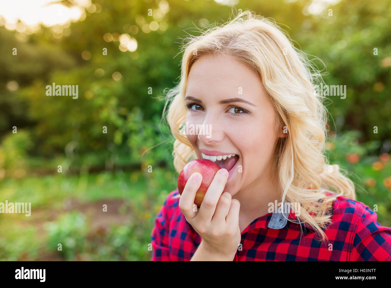 Bella donna bionda in rosso controllato shirt mangiare apple Foto Stock
