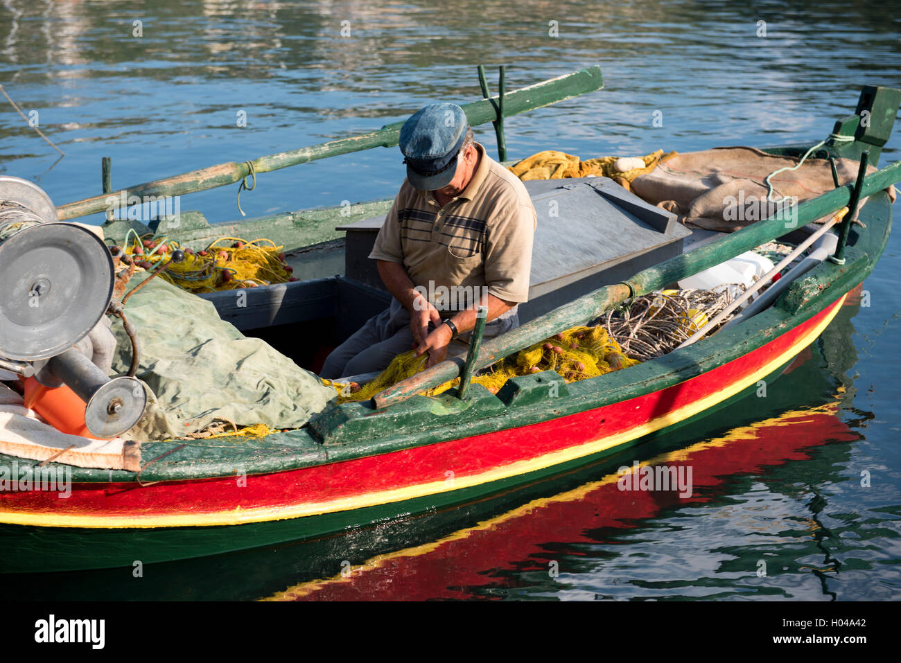 Un pescatore lavorando sulle sue reti in un colorato vecchia barca nel porto di Gaios a Paxos, Isole Ionie, isole greche, Grecia Foto Stock