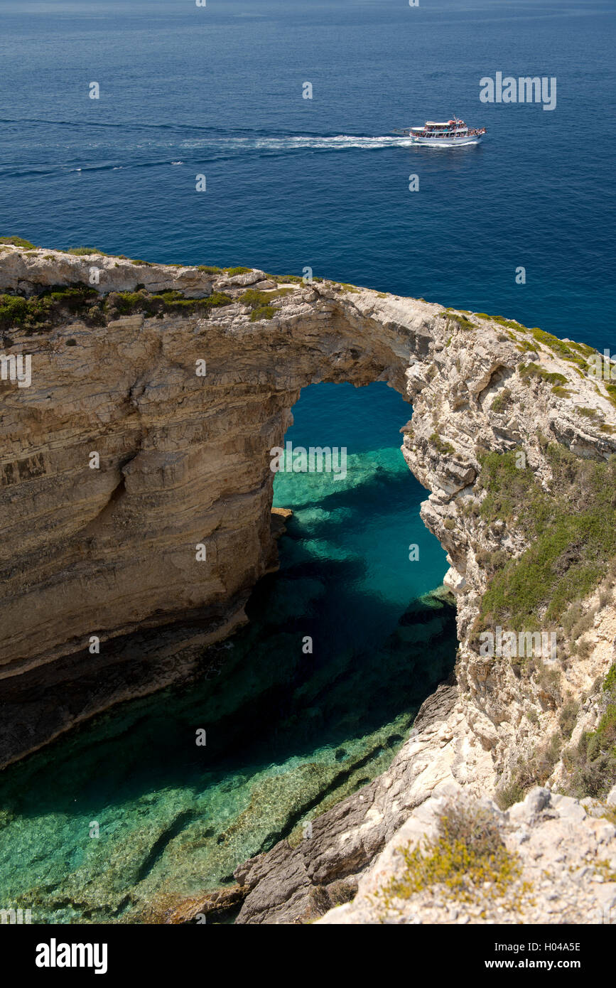 Un'escursione in barca passando il Trypitos Arch, un arco calcareo sul mare sulla costa occidentale di Paxos, le isole greche Foto Stock