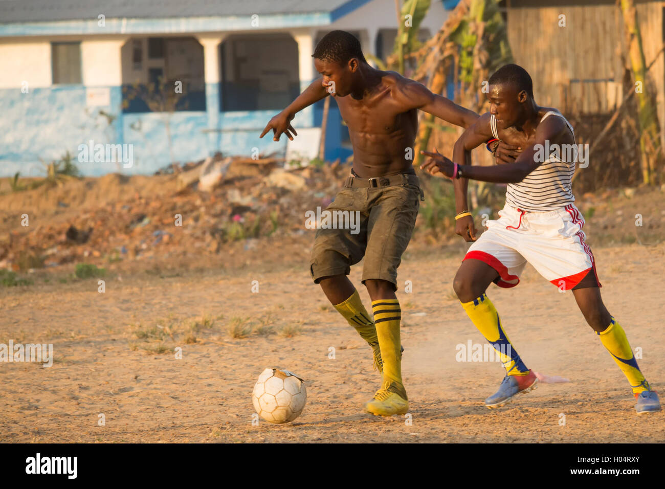 Due giovani uomini che giocano a calcio / calcio nel villaggio africano con vestito di stracci vecchi sfera Foto Stock