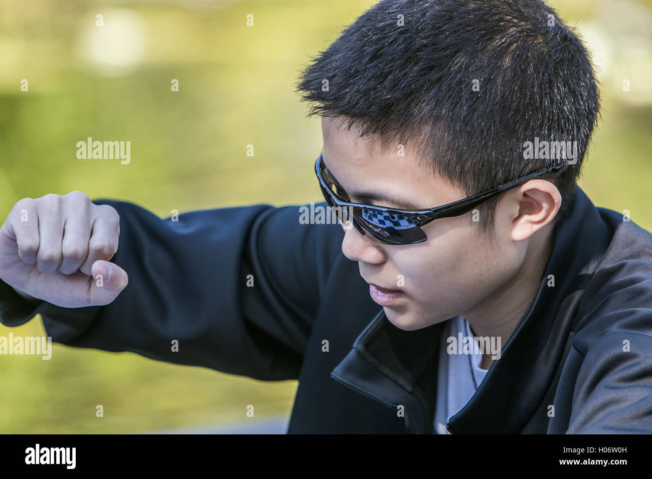 Un ragazzo sta facendo una mossa durante una partita a scacchi. La scacchiera è riflesso nei suoi occhiali da sole. Foto Stock