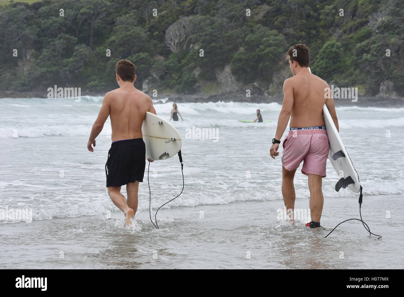 Due surfisti maschi che trasportano tavole da surf in acque poco profonde Foto Stock