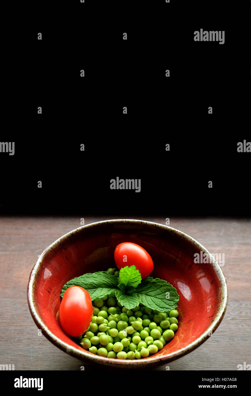 Fresco giardino piselli con la menta e pomodori in mano-gettato la coppa in ceramica Foto Stock