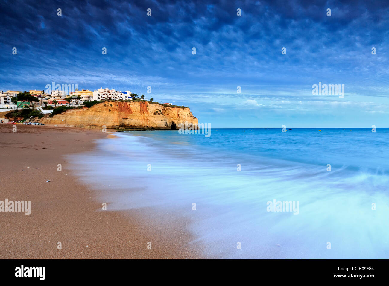 Oceano onde che si infrangono sulle rocce e spiaggia che circonda il villaggio di Carvoeiro al tramonto, Lagoa comune, Algarve, Portogallo, Europa Foto Stock