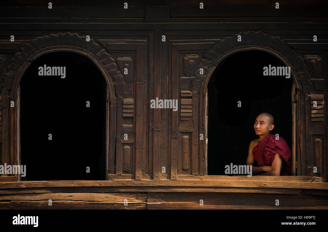 Un monaco guarda fuori dalla finestra di un monastero in legno vicino a Bagan (pagano), Myanmar (Birmania), Asia Foto Stock