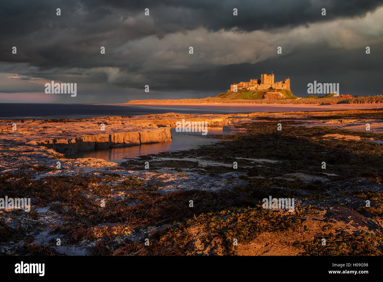 Una tempesta passa dietro il castello di Bamburgh con la luce del giorno illuminando la costa rocciosa e il castello, Northumberland, Regno Unito Foto Stock
