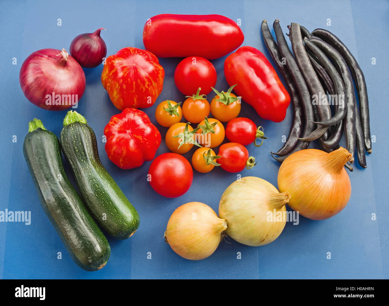 La disposizione di un assortimento di varietà di raccolti di fresco i pomodori e altri giardino estivo di verdure, su uno sfondo blu. Foto Stock