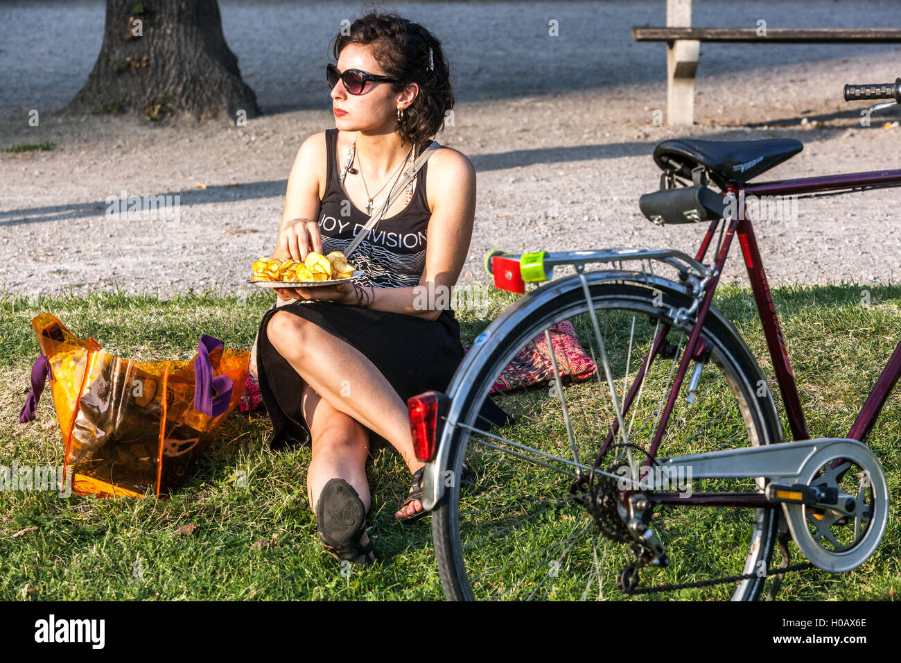 Giovane donna seduta nel parco e mangiare patatine, Augarten, Vienna, Austria donna bicicletta stile di vita città Foto Stock