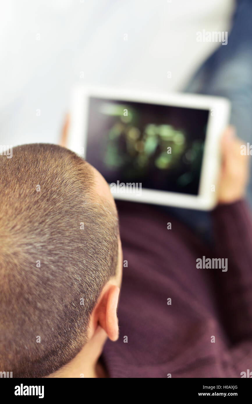 Un giovane uomo caucasico sdraiato sul divano guardando un film o una serie in streaming nel suo computer tablet Foto Stock