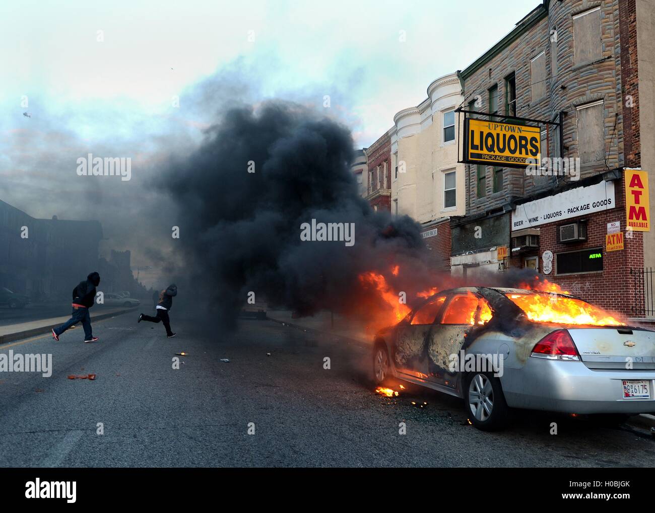 Due uomini che scorrono attraverso la strada di distanza da un ardente auto incendiate durante disordini dopo il funerale di Freddie Gray 27 aprile 2015 a Baltimora, Maryland. Grigio morì dalle ferite subite mentre in custodia della polizia. Foto Stock