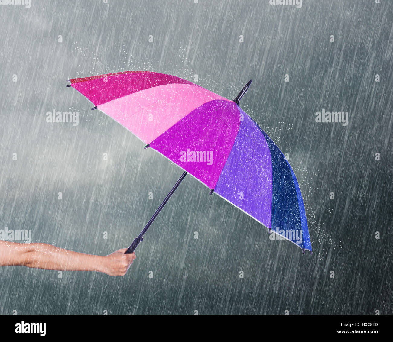 Mano azienda ombrello multicolore sotto il cielo scuro con la caduta di pioggia Foto Stock