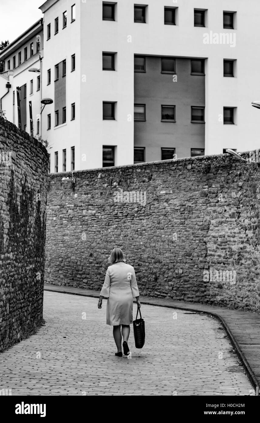 Donna che cammina lungo una città back street con alte mura, England, Regno Unito Foto Stock