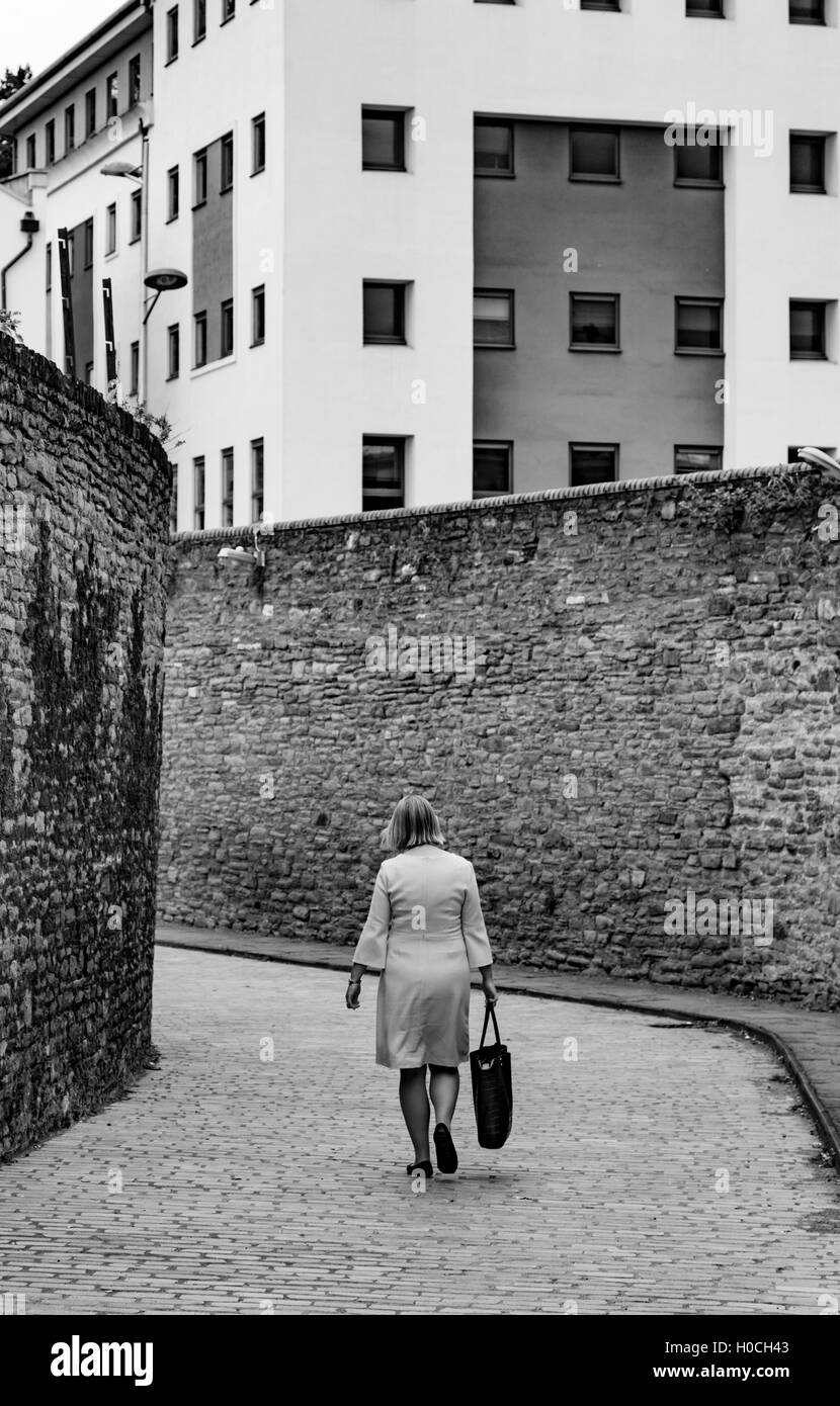 Donna che cammina lungo una città back street con alte mura, England, Regno Unito Foto Stock