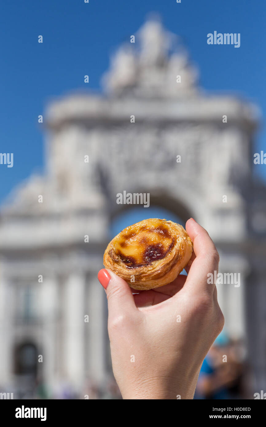 Tradizionale portoghese crostata di uovo pastoso dessert torta Pasteis de nata in mano alle donne. Sullo sfondo le attrazioni di Lisbona, Portogallo. Foto Stock