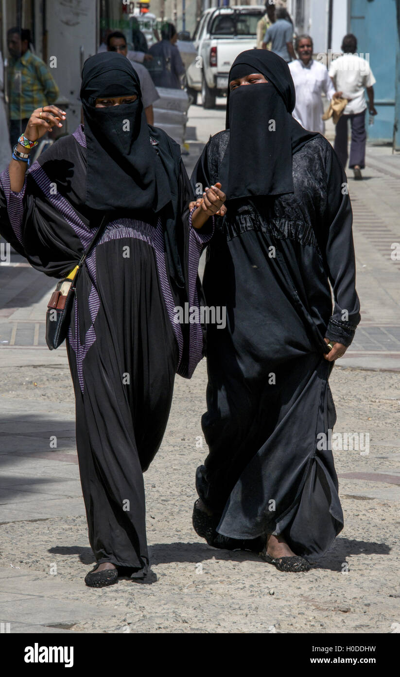 Due donne coperte nel tradizionale abayas nero a piedi attraverso le strade di Jeddah, Arabia Saudita Foto Stock