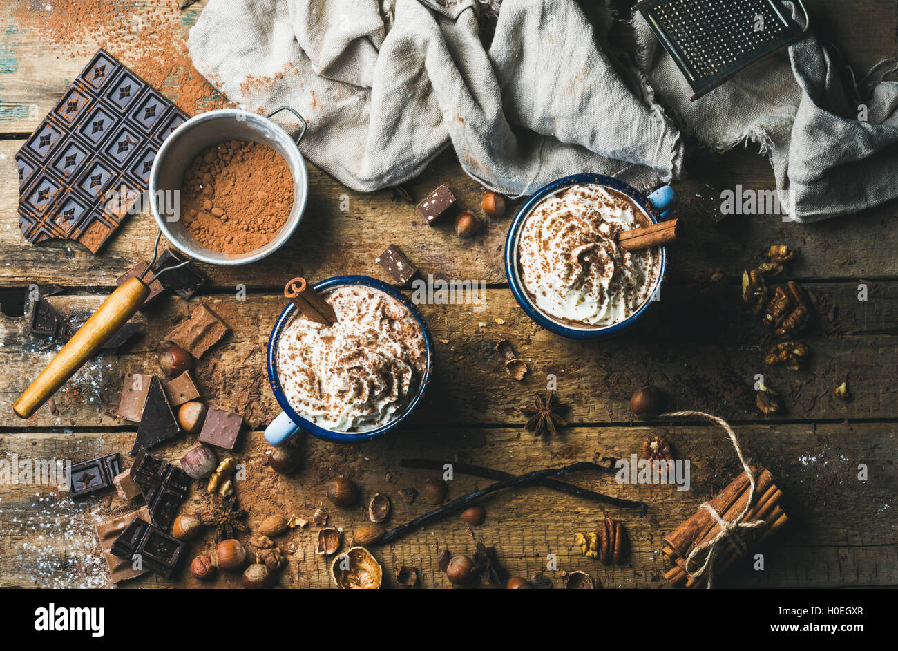 Cioccolata calda con panna montata, noci e cannella in smalto tazze con ingredienti intorno sul legno rustico sfondo, vista dall'alto Foto Stock