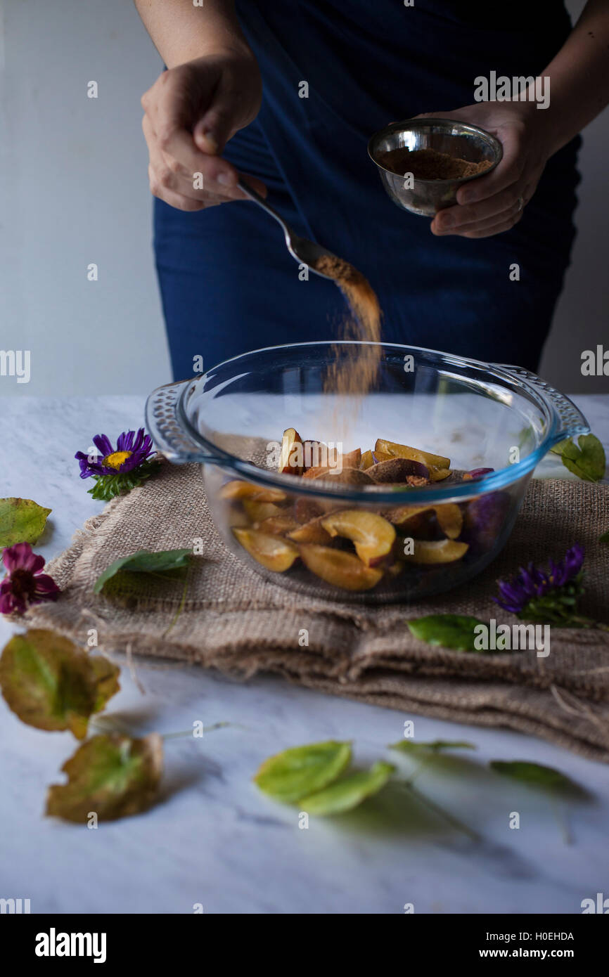 Donna spolverata di zucchero di cocco sulle fette di prugne, ingredienti per la cottura in forno di prugna galette Foto Stock
