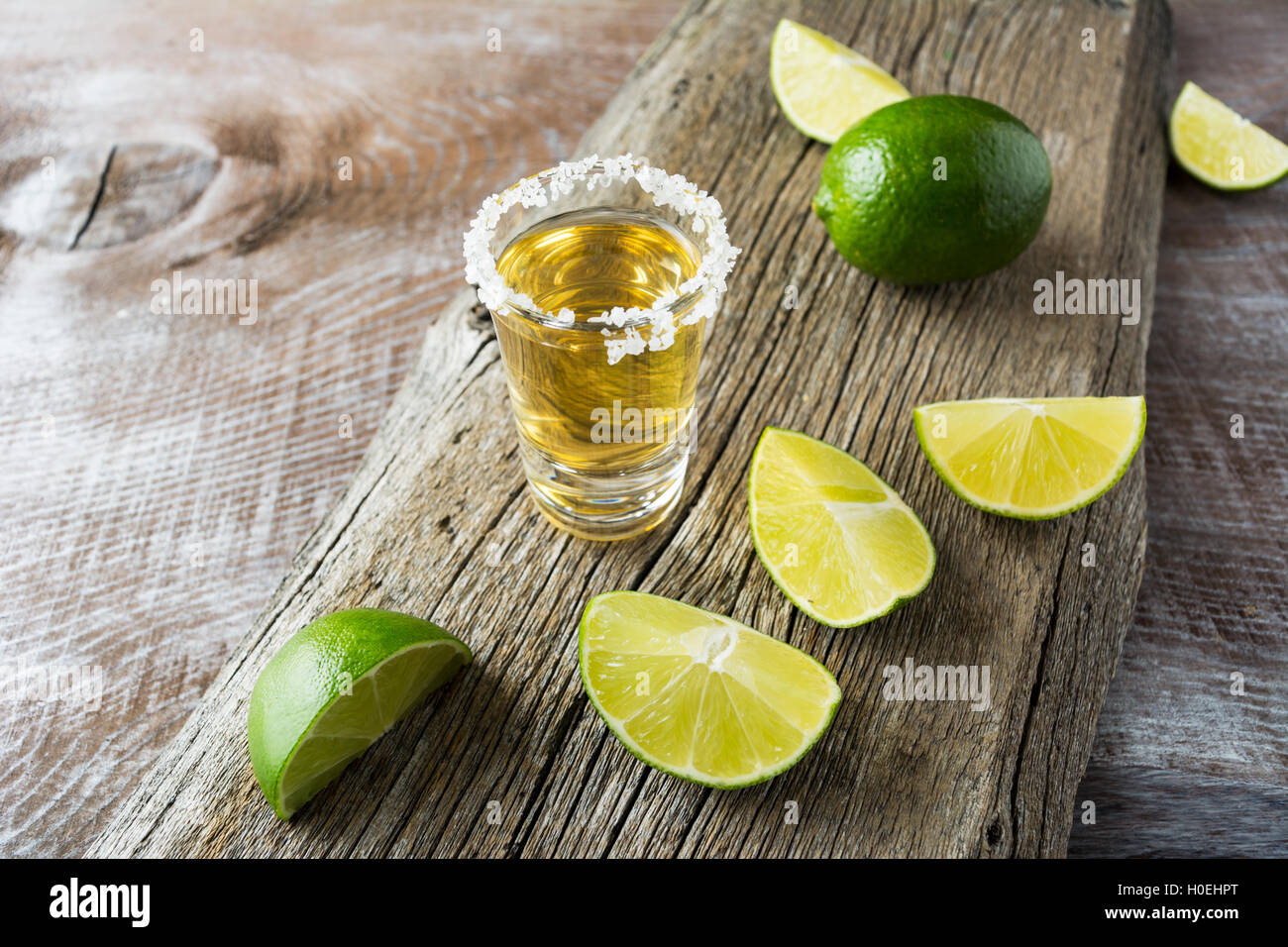 Tequila shot con fettine di lime sul legno rustico sfondo. Forte bere alcool. Oro tequila messicana shot. Foto Stock