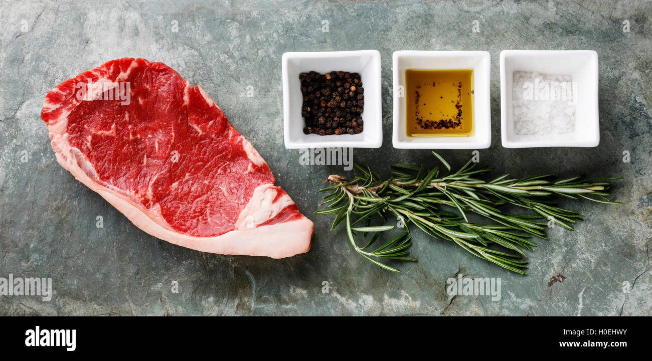 Materie carni fresche bistecca di controfiletto al rosmarino, olio, sale e pepe in pietra sullo sfondo di ardesia Foto Stock