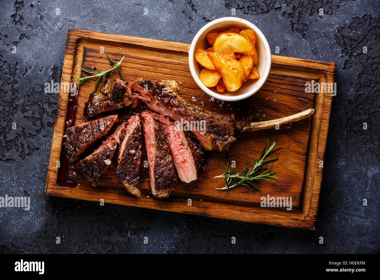 Fette di mezzo raro barbecue Steak su ossa bovine nervatura con spicchi di patate su sfondo scuro Foto Stock