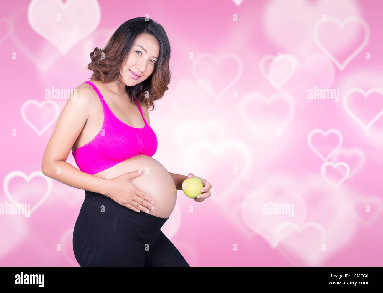 Bella donna incinta con mela verde su sfondo di cuore Foto Stock