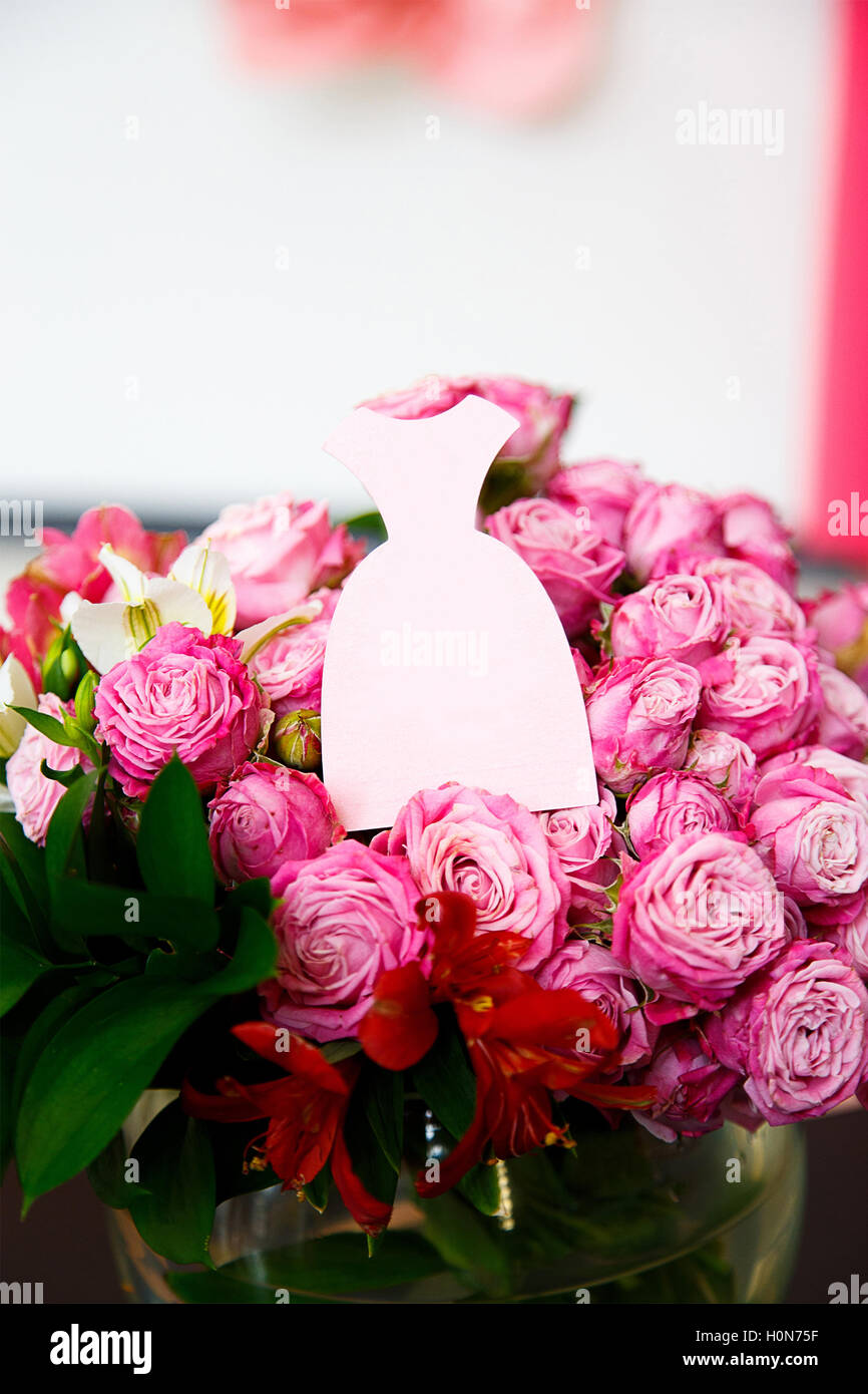 Una carta in forma di abito rosa su bouquet di rose rosa Foto Stock