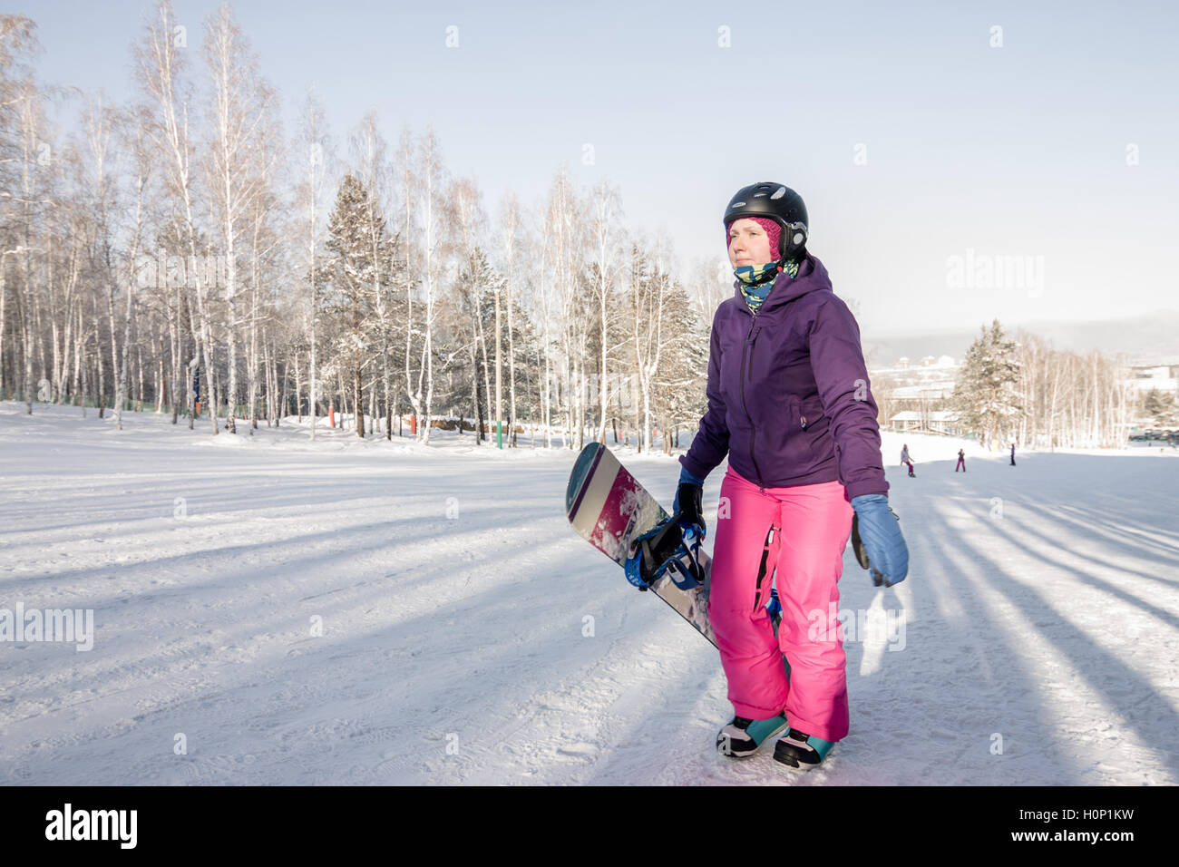 Ragazza in viola giacca e pantaloni rosa con lo snowboard nelle mani della salita in inverno Foto Stock