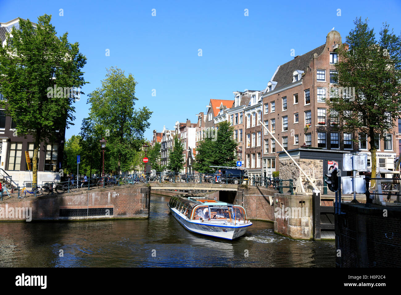 Imbarcazione turistica passa sotto uno dei ponti sui canali di Amsterdam Foto Stock